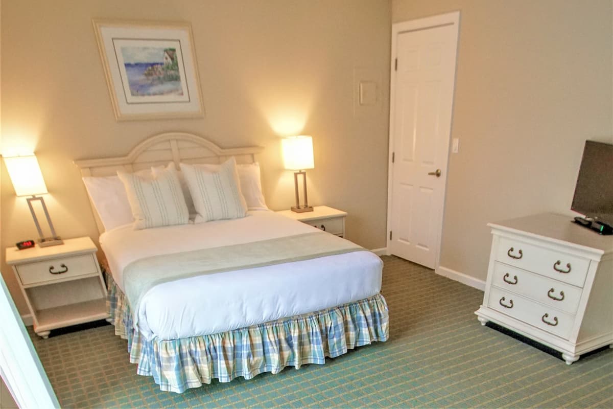 Une chambre à coucher bien rangée, avec un lit, des lampes de chevet, une commode et une porte.