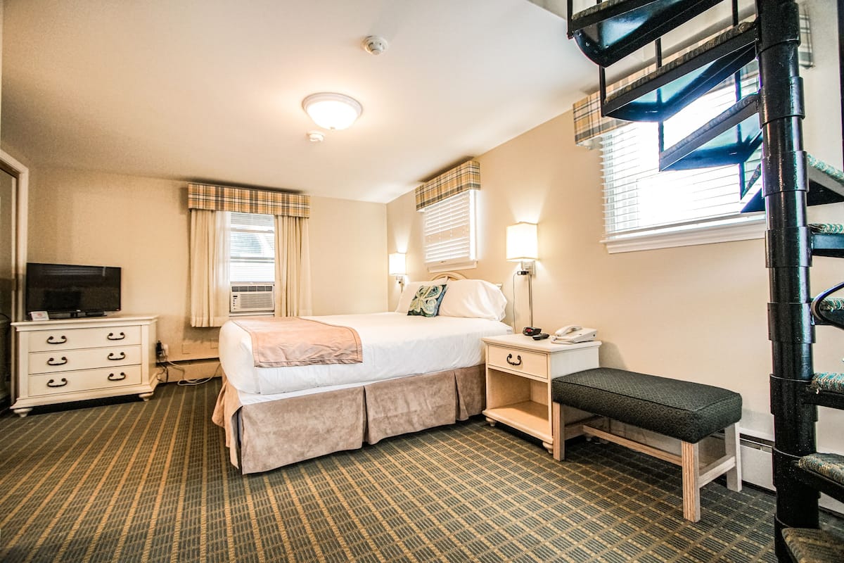 Une chambre d’hôtel comprenant un lit, une table de chevet, une lampe, une chaise, une commode et un téléviseur.