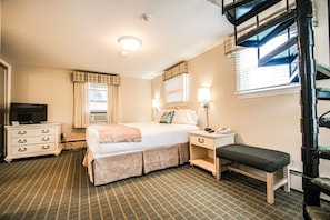 A hotel room with a bed, bedside table, lamp, chair, dresser, and a TV.