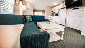 A compact living space with a sofa, a coffee table, a television, and a kitchenette. - Cape Winds Resort (Hyannis)