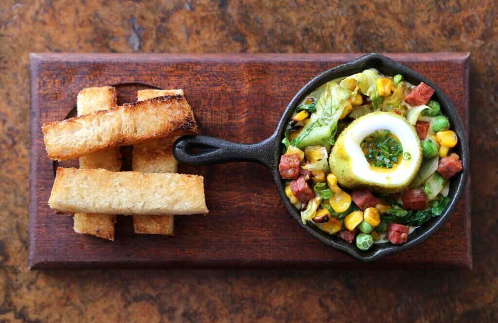 Una sartén con un plato de vegetales y huevo de colores, acompañado de pan tostado sobre una tabla de madera.