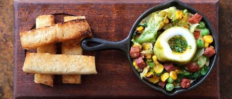 Una sartén con un plato de vegetales y huevo de colores, acompañado de pan tostado sobre una tabla de madera.