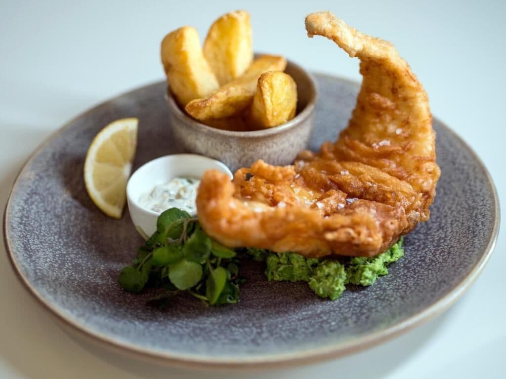 A plate with a piece of fried fish, lemon wedges, and a small bowl of tartar sauce.