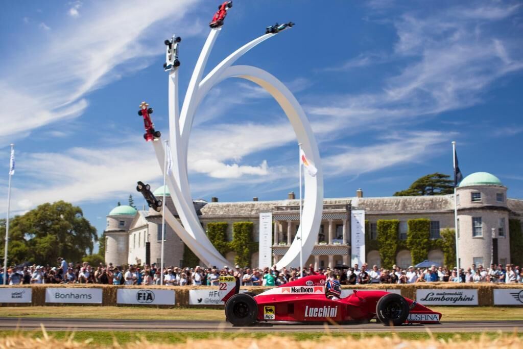 A red race car on a track with spectators and a building in the background.
