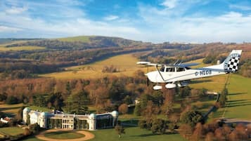 A small white aircraft with the registration G-HLOB flying over a large estate with a distinctive building featuring domed towers.