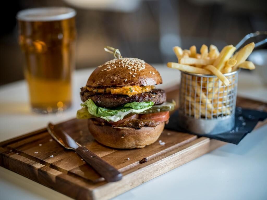 A burger with fries and a beer on a wooden board.