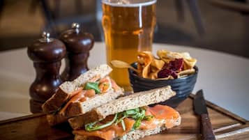 A sandwich with smoked salmon, a glass of beer, and a bowl of chips on a wooden board.
