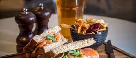 Un sándwich de salmón ahumado, una jarra de cerveza y un bol de papas fritas sobre una tabla de madera.
