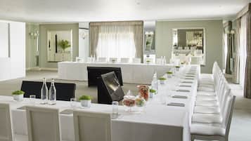 A long dining table set with chairs, a projector screen, and various table settings including glassware and small plants.