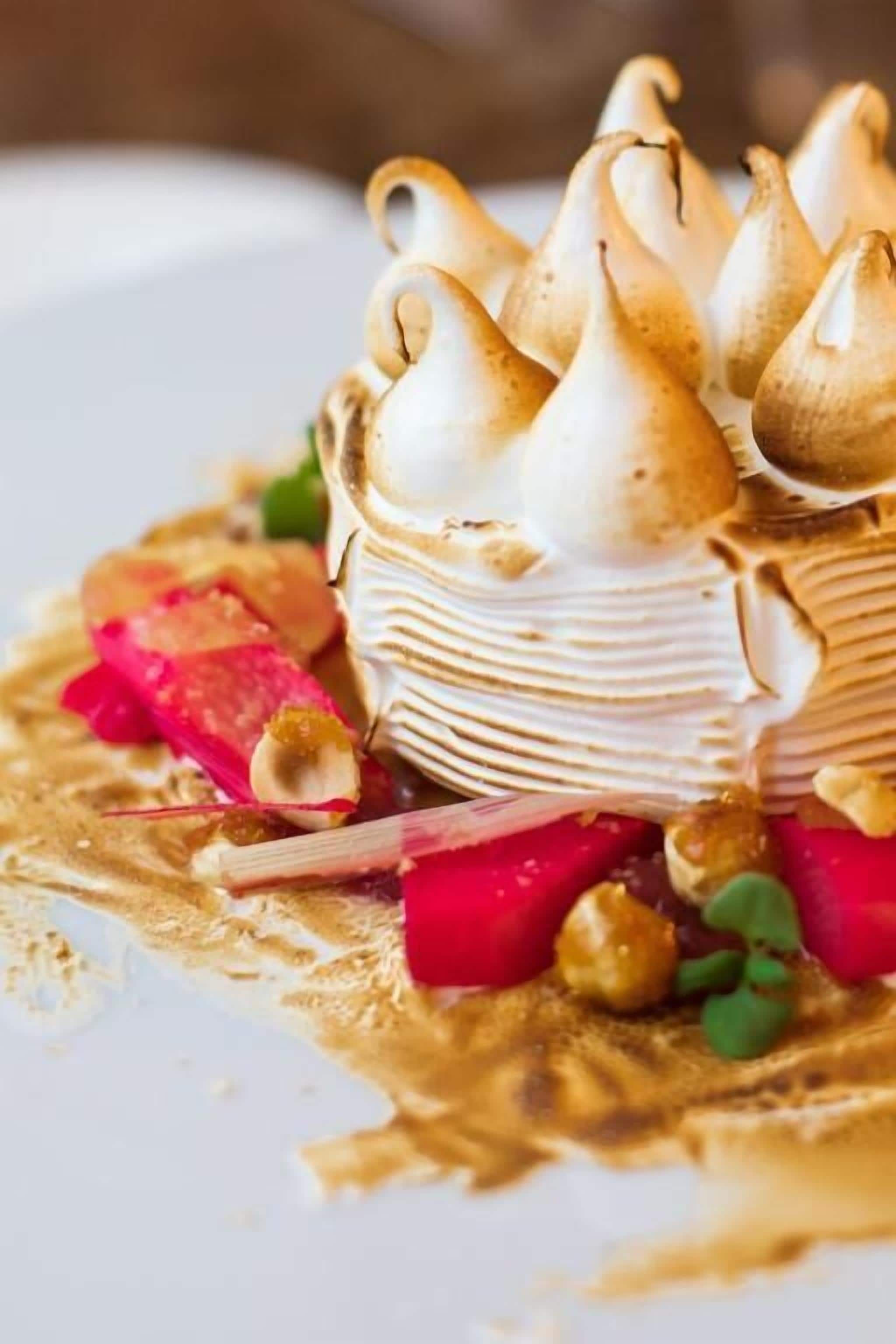 A dessert with meringue peaks and a layered base, garnished with red and green elements.