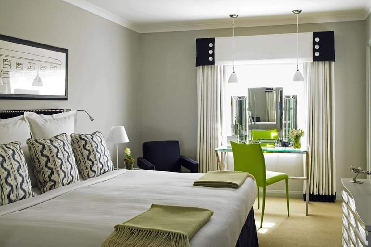 A hotel room with a large bed, a desk, a chair, a mirror, and a television.