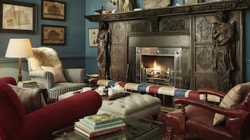 Un salón acogedor con chimenea, sillones a rayas, un sofá rojo y una mesa de centro de cristal con libros.