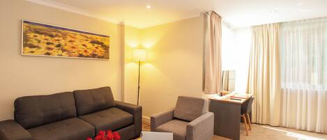 A hotel room with a sofa, armchair, desk, and laptop.