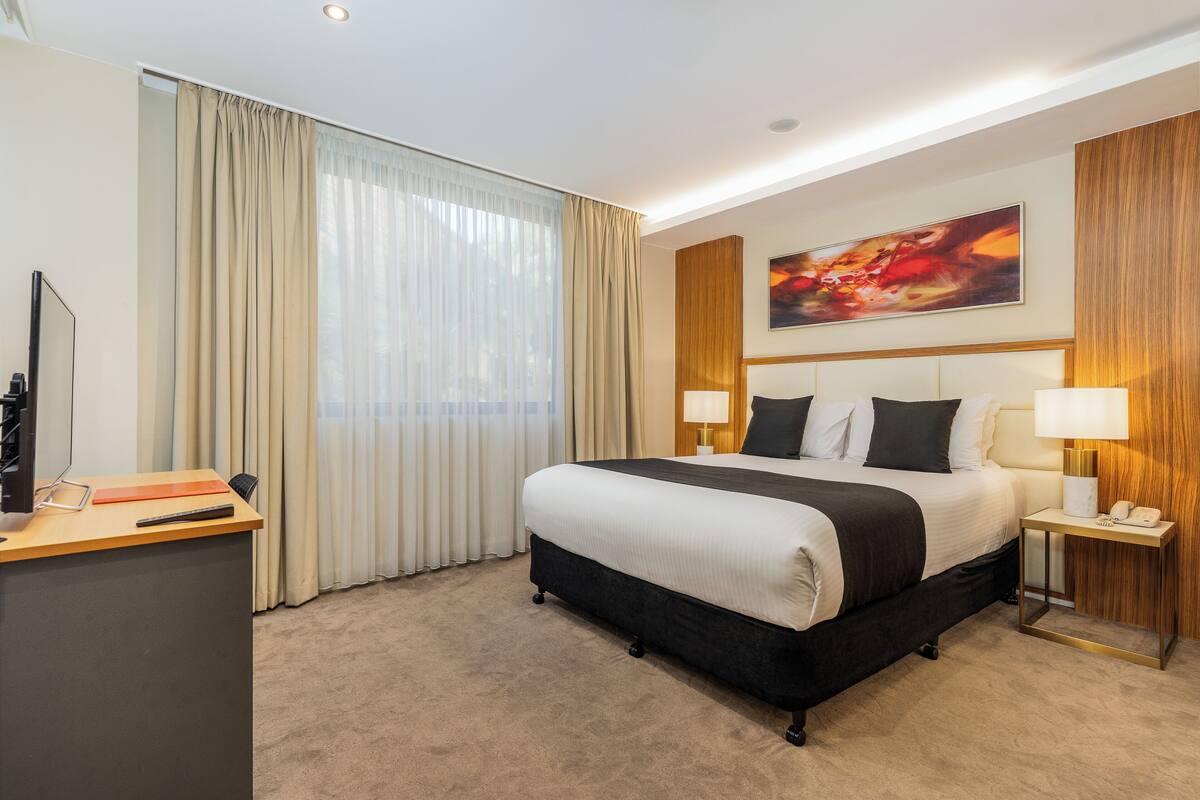 A hotel room with a large bed, a desk with a computer, and a painting on the wall.