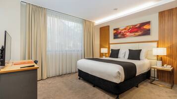 A hotel room with a large bed, a desk with a computer, and a painting on the wall.