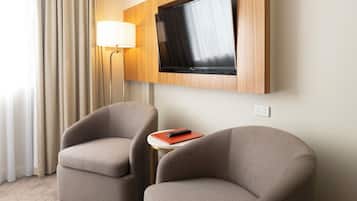 Une chambre d’hôtel avec deux fauteuils, un téléviseur fixé au mur, une lampe et une petite table avec une télécommande.