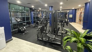 A gym with various exercise equipment, large windows, and a blue accent wall. - Hotel Diana Woolloongabba (Woolloongabba)