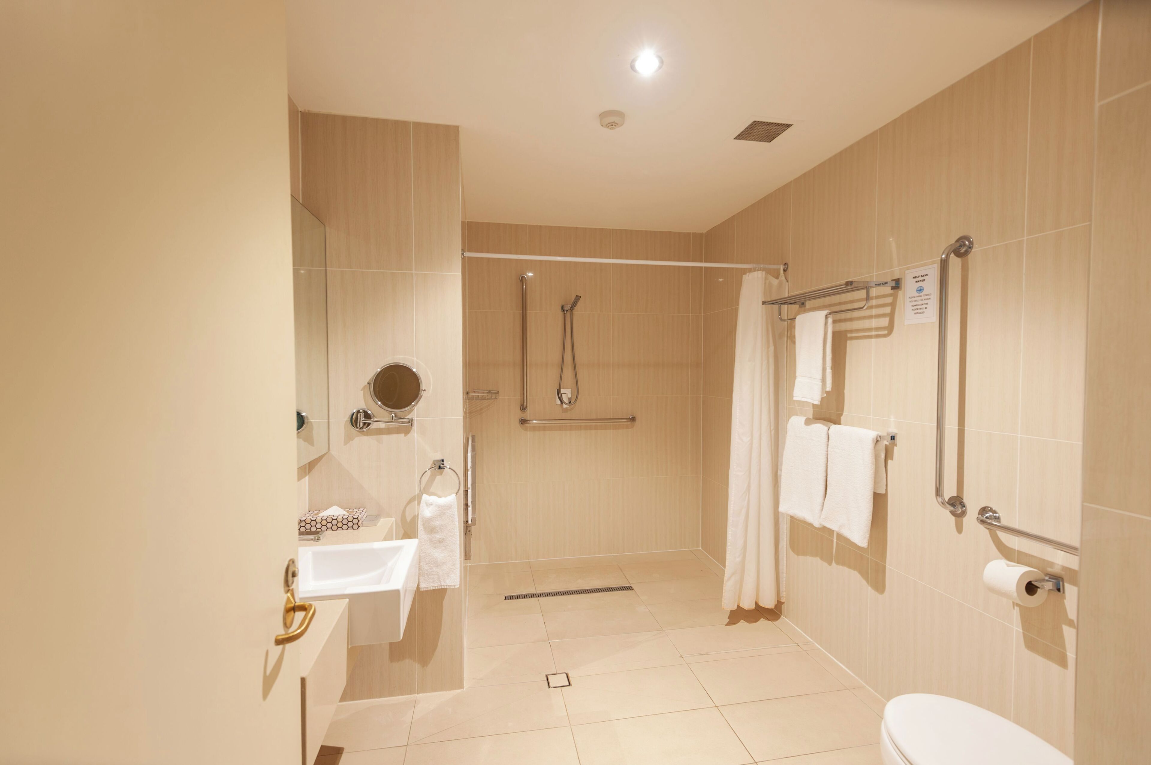 Un baño moderno con ducha, inodoro, lavamanos y barras de apoyo.