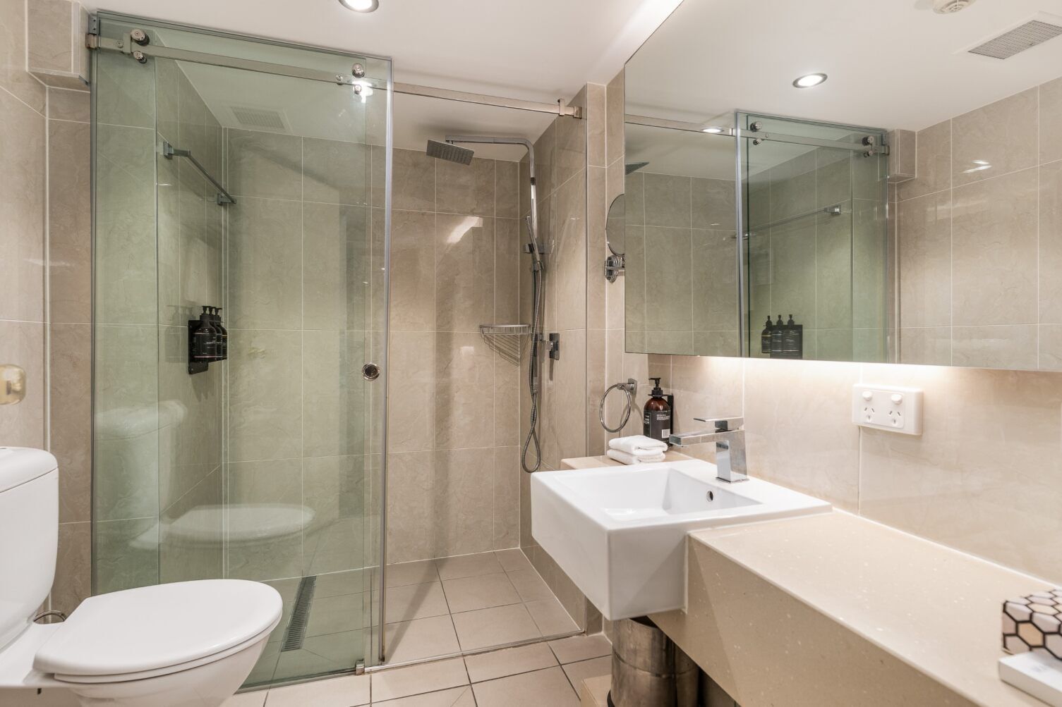 Un baño moderno con cabina de ducha de vidrio, un lavabo blanco y un inodoro.