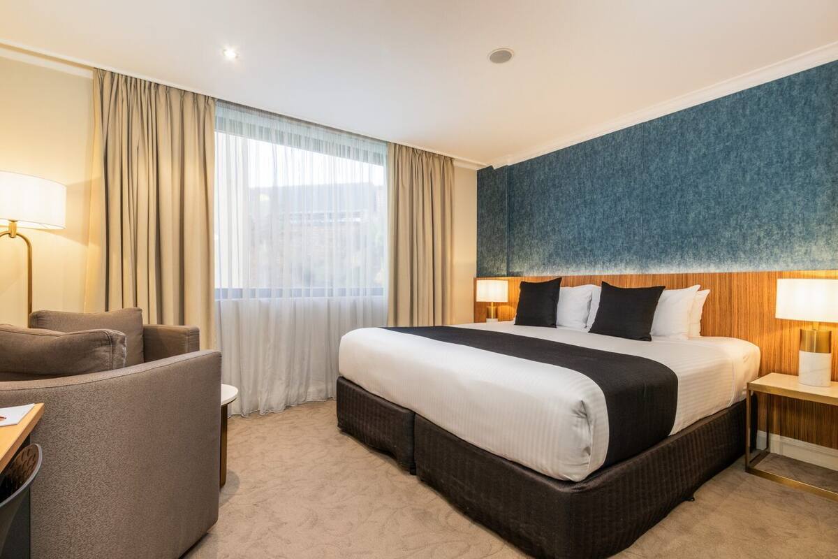 A hotel room with a large bed, a sofa, a desk, and a window with curtains.
