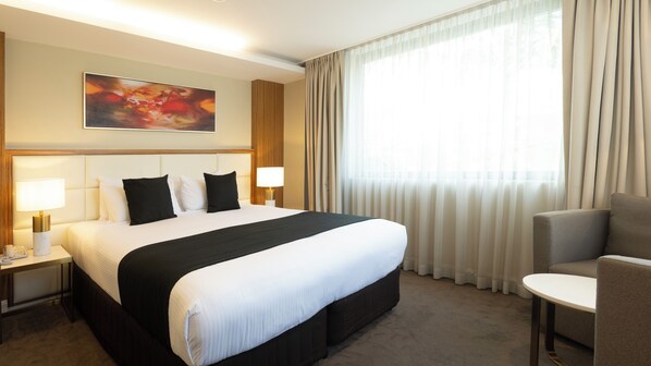 A hotel room with a large bed, two bedside lamps, a chair, and a painting on the wall.