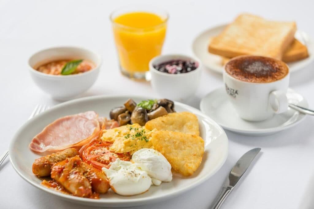 A breakfast plate with eggs, bacon, mushrooms, tomatoes, and toast, accompanied by a glass of orange juice and a cup of coffee.
