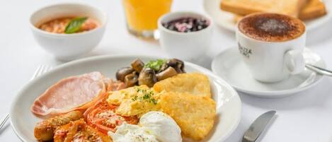 A breakfast plate with eggs, bacon, mushrooms, tomatoes, and toast, accompanied by a glass of orange juice and a cup of coffee.