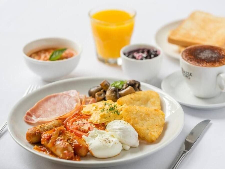 A breakfast plate with eggs, bacon, mushrooms, tomatoes, and toast, accompanied by a glass of orange juice and a cup of coffee.