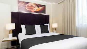Een hotelkamer met een groot bed, twee bedlampen, een donker hoofdeinde en een ingelijst schilderij boven het bed.