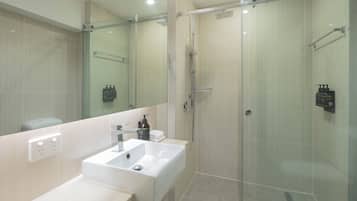 Uma casa de banho moderna com cabine de duche em vidro, lavatório branco e espelho grande.