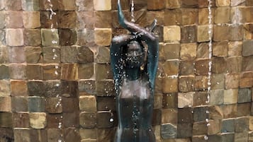A bronze statue of a woman with water flowing from her head, set against a mosaic wall.