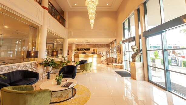 A spacious lobby with a chandelier, seating areas, a reception desk, and large windows. - Hotel Diana Woolloongabba (Woolloongabba)