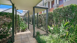 A covered outdoor corridor with a tiled pathway, surrounded by greenery and modern buildings.