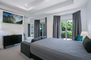 A modern bedroom with a large bed, a black dresser, a painting, and a view of greenery through the windows. - Comfort Inn & Apartments Northgate Airport (Northgate)
