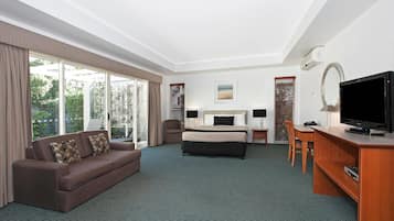 A hotel room with a bed, a sofa, a desk, a television, and large windows.