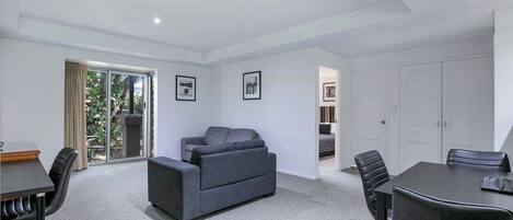 A modern room with a grey sofa, a dining table with chairs, and a sliding glass door leading to a balcony.
