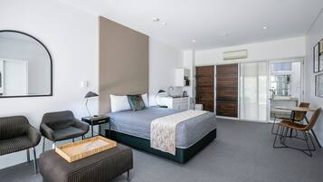 A modern hotel room with a large bed, a desk, two chairs, a small table, and a mirror.