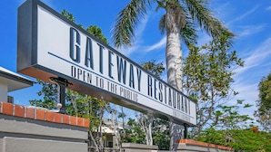 A sign for a Gateway Restaurant with a clear sky and palm trees in the background.