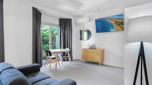 A modern room with a grey sofa, a dining table with chairs, a wooden cabinet, and a large window with curtains.