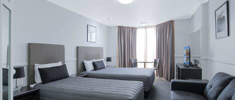 A hotel room with two beds, a sofa, a desk, and a chair.