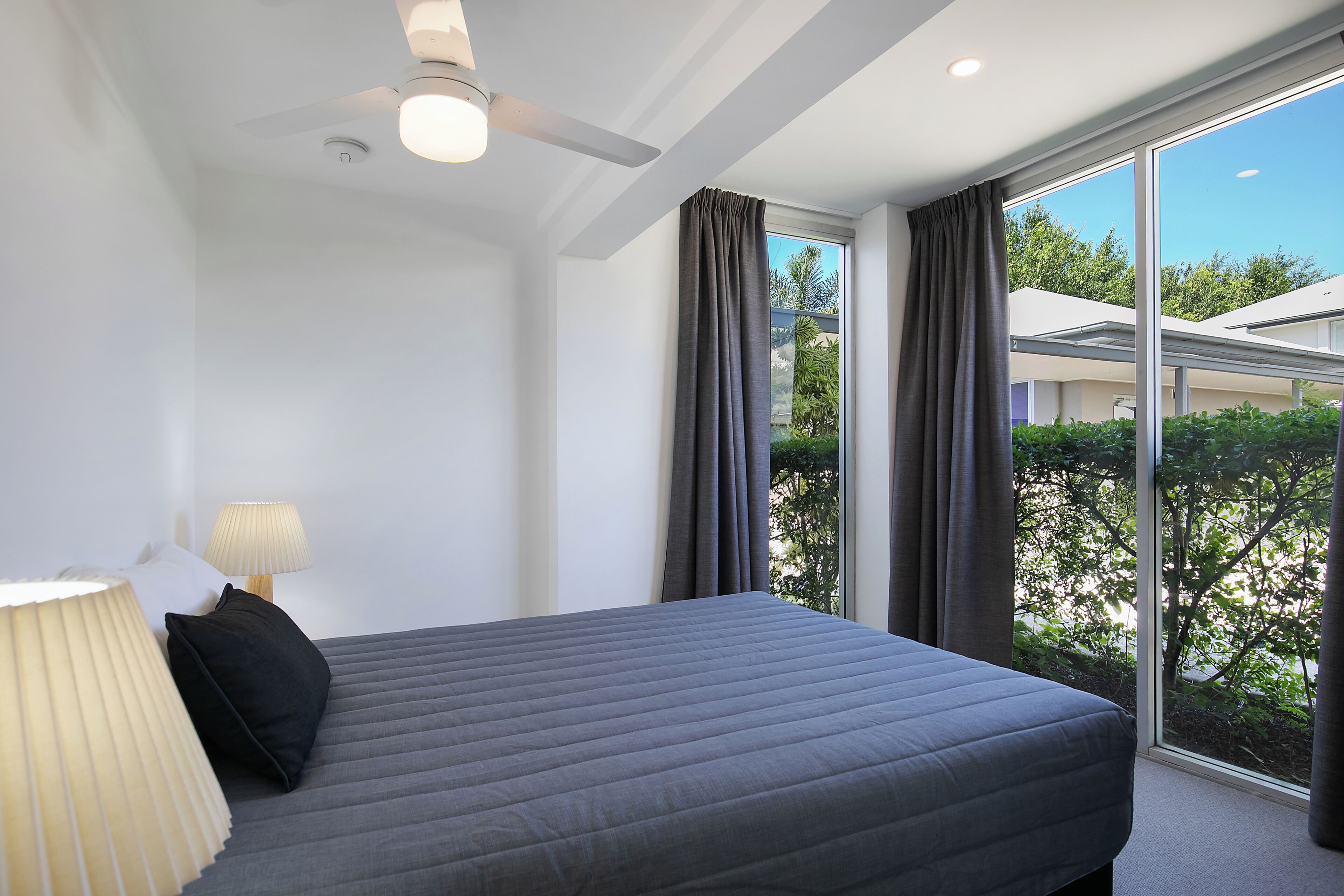 Un dormitorio moderno con una cama grande, ventilador de techo y vista a zonas verdes.