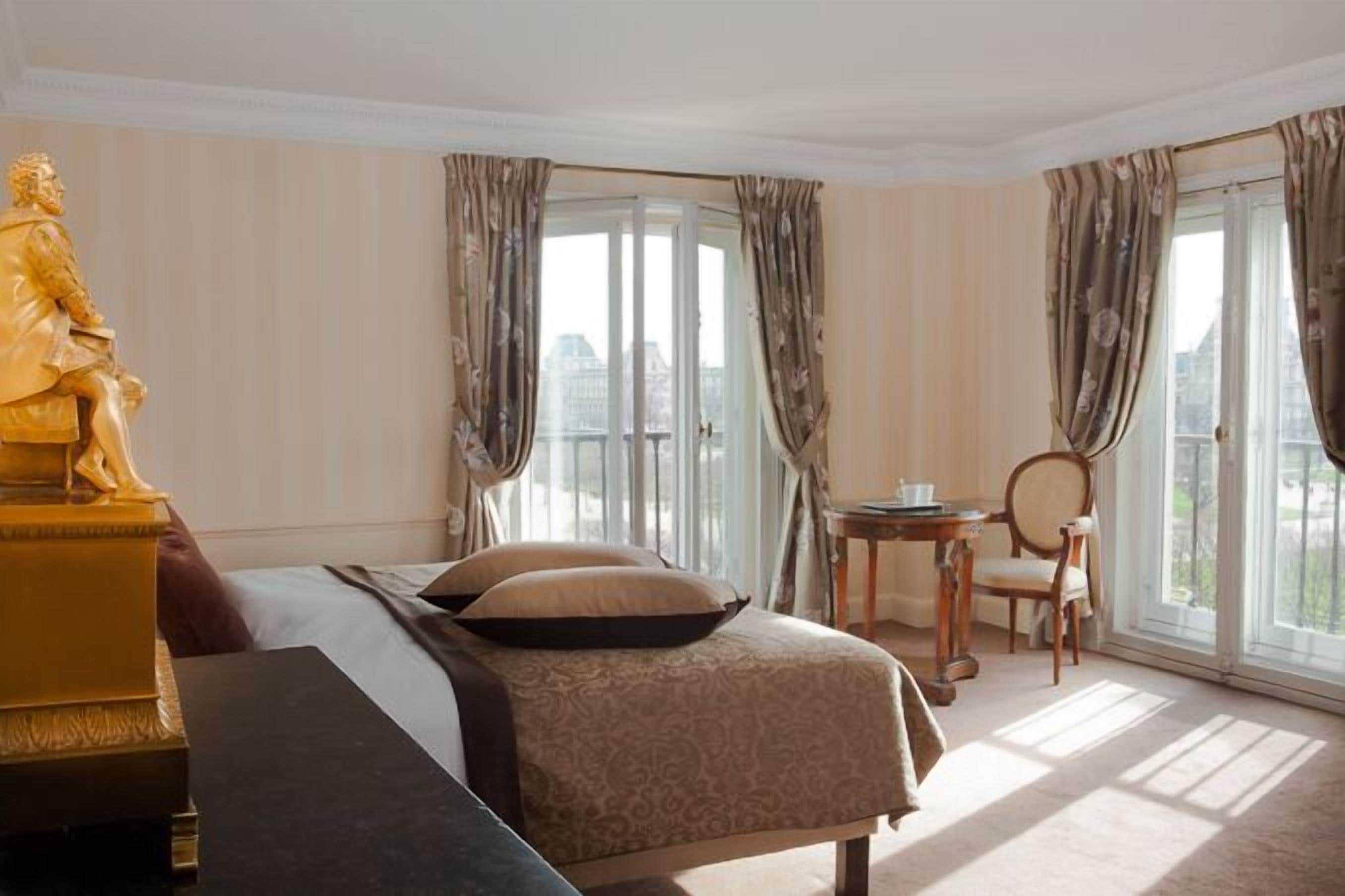 A hotel room with a bed, a statue, a small table, and a chair.