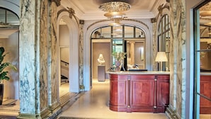 A grand hallway with marble columns, a central wooden reception desk, and a large mirror reflecting the space. - Hotel Brighton (Paris)