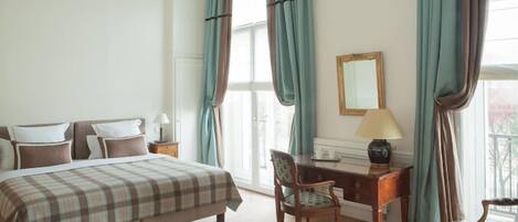 A hotel room with a bed, a desk, a chair, a lamp, and curtains.