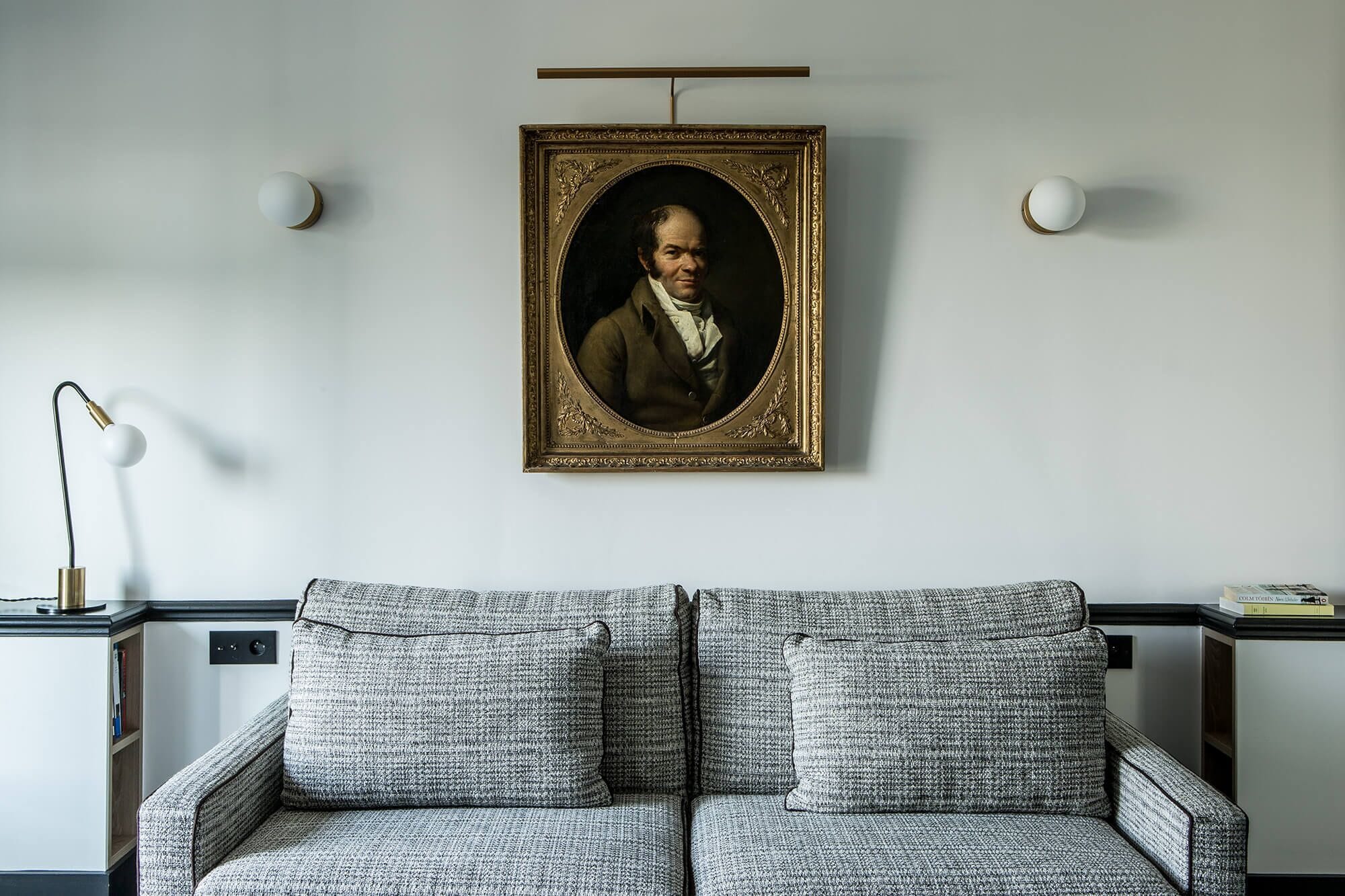 A room with a patterned sofa, a framed portrait on the wall, and a lamp on a side table.