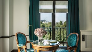 A room with a view of a cityscape, featuring a table with a vase of flowers, two chairs, and a radiator. - Hotel Brighton (Paris)
