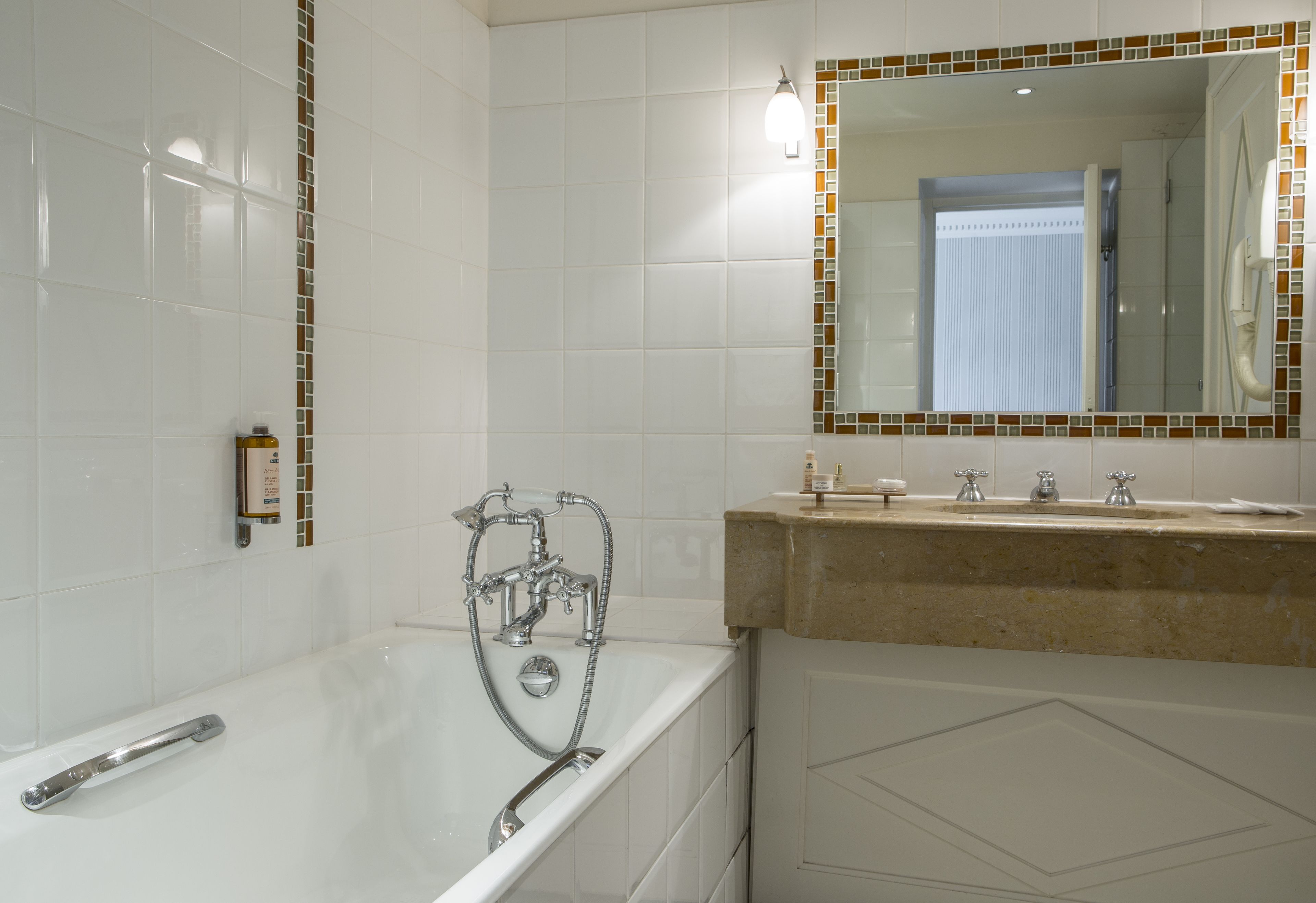 Ein Badezimmer mit einer Badewanne, einem Waschbecken und einem Spiegel mit Mosaikbordüre.