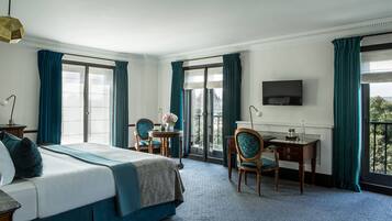 Ein Hotelzimmer mit einem Bett, zwei Stühlen, einem Schreibtisch, einem Fernseher und großen Fenstern mit Vorhängen.