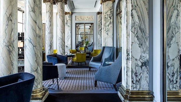A luxurious lobby with marble columns, a seating area with modern chairs, and a decorative mirror. - Hotel Brighton (Paris)