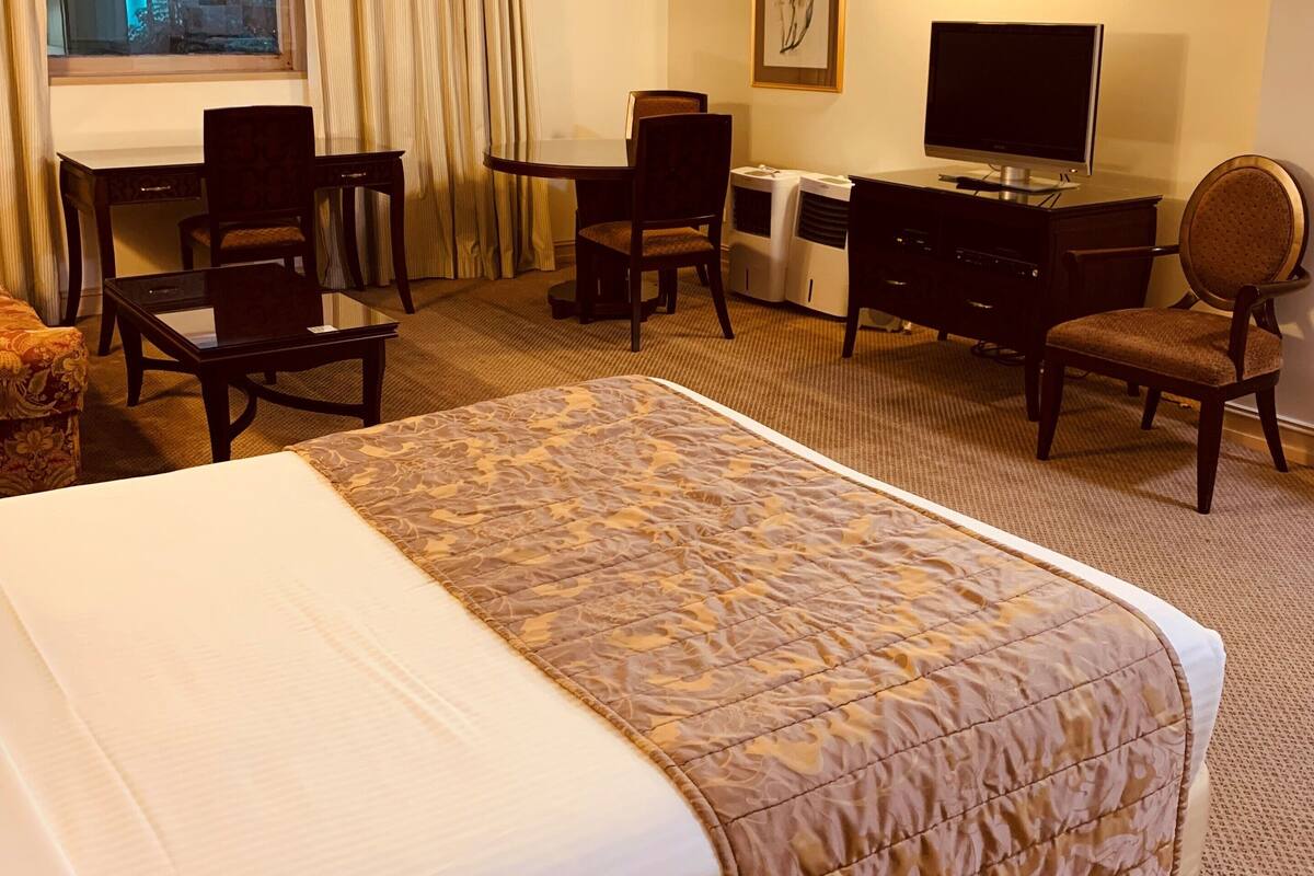 A hotel room with a large bed, a desk with a chair, a television, and a window with curtains.